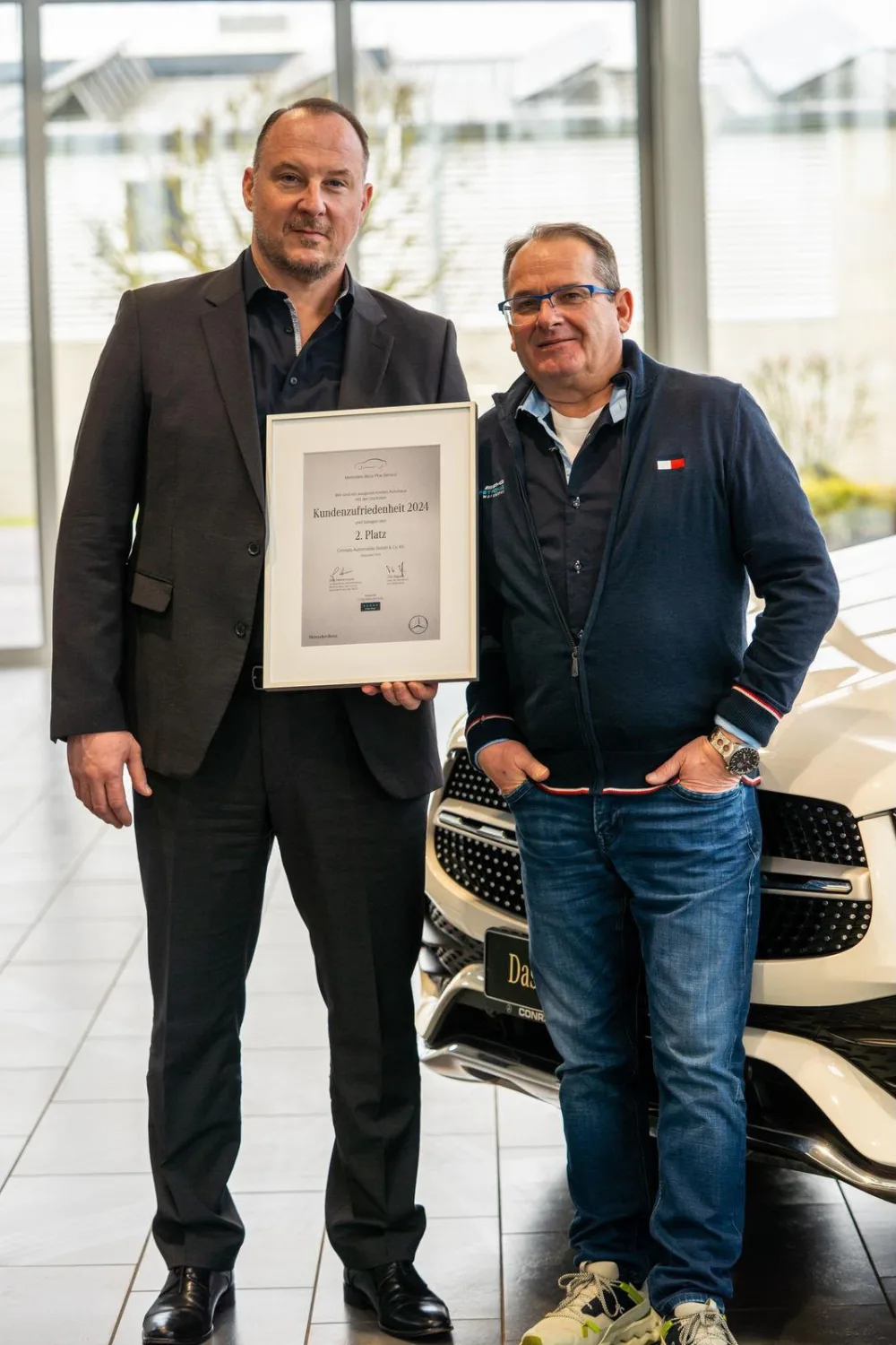 Zwei Mitarbeiter von Conrady Automobile mit der gerahmten Urkunde der Mercedes-Benz Kundenzufriedenheitsstudie 2024