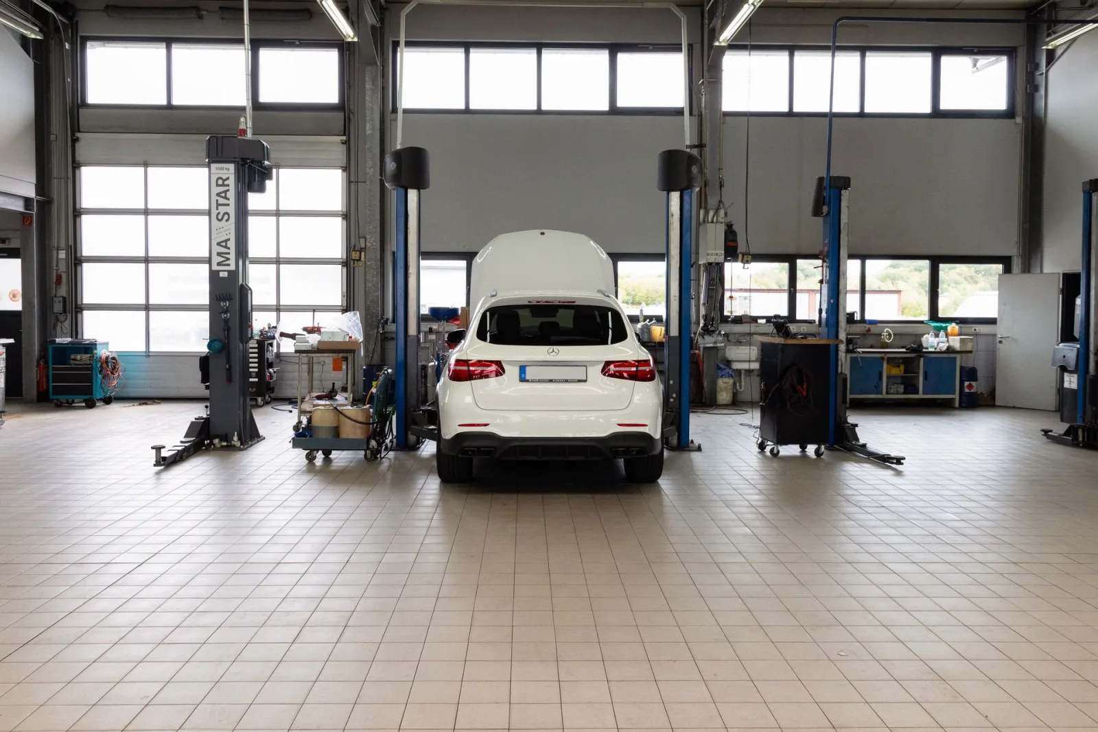 Werkstatthalle von Conrady Automobile in Bitburg: ein weißer Mercedes zwischen zwei Hebebühnen, dahinter Werkbänke und Hallenfenster